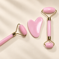 Set rosa de rodillos faciales y gua sha sobre fondo crema